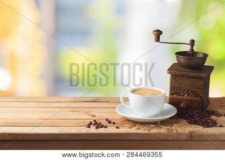 Coffee Cup With Grinder Mill On Wooden Table Over Abstract Bokeh Background With Copy Space