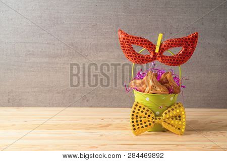Jewish Holiday Purim Background With Bucket, Carnival Mask And Hamantaschen Cookies On Wooden Table.
