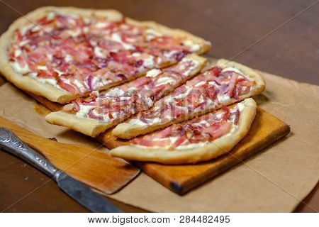 Alsatian Tart Flambé Or Flammkuchen With Bacon And Onions On A Dark Table.