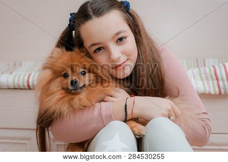 Teenage Girl With A Dog Breed Spitz Rejoices With A Pet At Home On The Floor. Care And Training Of A