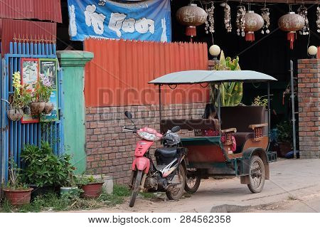 Cambodia, Siem Reap 12/08/2018 A Little Asian Girl Sits In A Moto Rickshaw Near A House With Red Lan