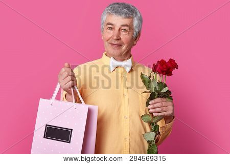 Handsome Elegant Man Wears Formal Outfit, Holds Giftbag And Bouquet Of Flowers, Going To Make Presen