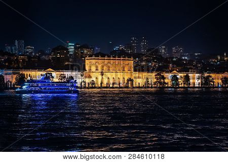 View Of The Dolmabahche Palace In Beams Of Night-time Lighting. Skyscrapers Of Modern Istanbul At A 