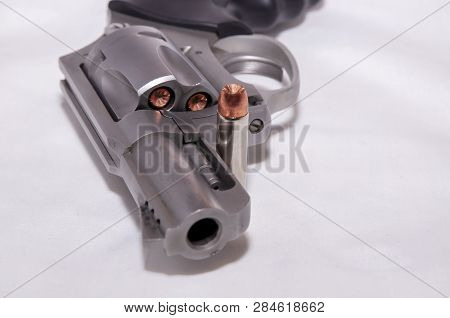 A Stainless 357 Magnum Revolver With A Single Bullet Next To It Shown On A White Background