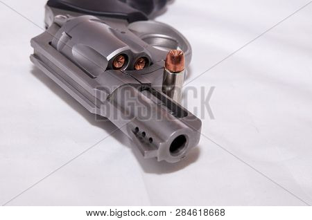 A Stainless 357 Magnum Revolver With A Single Bullet Next To It Shown On A White Background