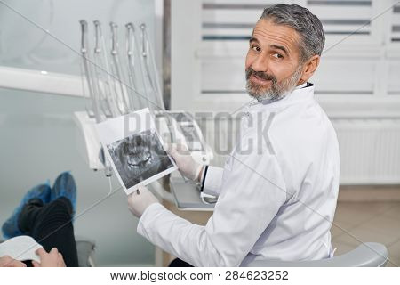 Professional, Cheerful Doctor Of Dentistry Clinic Sitting In Chair. Bearded, Handsome Dentis Looking