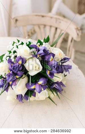 Beautiful Wedding Bouquet Of Fresh Violet Irises And White Roses On A White Table.