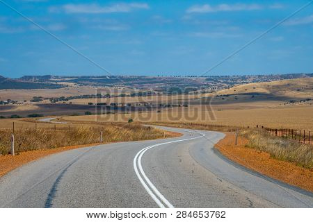 Australian Bush Road Curving Through Dry Landscape With Corn Fields