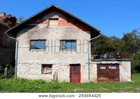 Suburban Family Brick House With Attached Garage And Cracked Damaged Facade From Shrapnels And Bulle