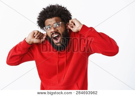 Studio Shot Of Disturbed Guy Suffering From Discomfort As Compaining On Loud Neighbours Being Irrita