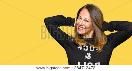 Beautiful middle age woman wearing rock and roll sweater Relaxing and stretching with arms and hands behind head and neck, smiling happy