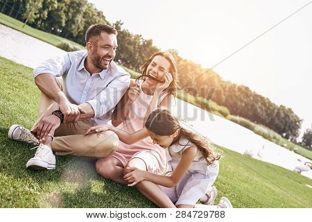 Bonding, Family Of Three Sitting On Grassy Field Having Fun Laug