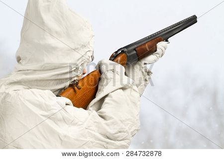 Hunter In White Camouflage Aims A Shotgun In The Winter