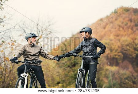 Active Senior Couple With Electrobikes Standing Outdoors On A Road In Nature.