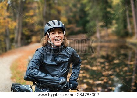 A Senior Woman With Electrobike Standing Outdoors On A Road In Park In Autumn.
