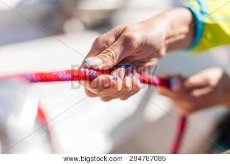 Holder of rope on sailboat, woman pulling rope. Detail of working crew on the deck. Low depth of focus.