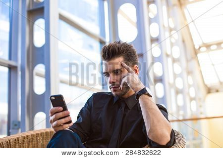 Confident Businessman Online Booking Via Mobile Phone, Sitting In Enterprise Hall. Serious Entrepren