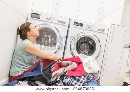 Upset Woman In Laudry Room Sitting Ona Floor With Dirty Clothes