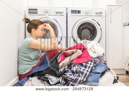 Upset Woman In Laudry Room Sitting Ona Floor With Dirty Clothes