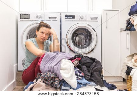Upset Woman In Laudry Room Sitting Ona Floor With Dirty Clothes