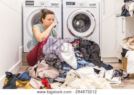 Upset Woman In Laudry Room Sitting Ona Floor With Dirty Clothes