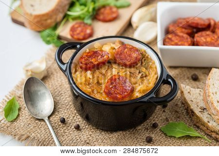 Slovak Christmas National Cabbage Soup In Two Small Black Pots With Sausage On The Jute Background.
