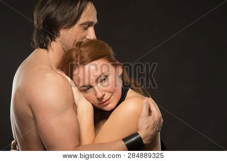 Safety. Relaxed Adorable Woman With Bare Shoulders Looking Away While Standing In Her Husbands Arms 
