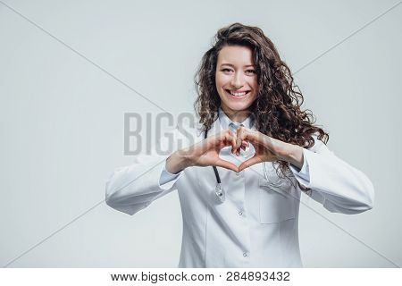 A Young Woman Doctor Is On A Gray Background. During This Time, The Heart Symbol Shows On The Chest 