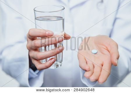 A Young Girl Doctor Takes Vitamins. At The Same Time, She Stands On A Gray Background Dressed In A W