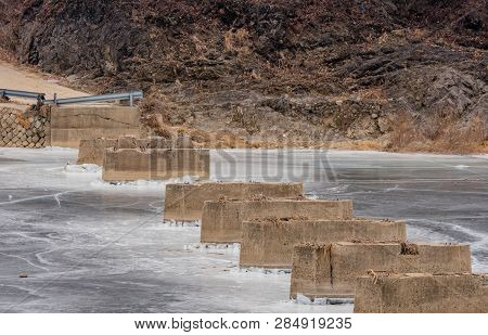 Concrete Column Plinths Of Unfinished Bridge Protruding Through Surface Of Frozen River On Gray Wint