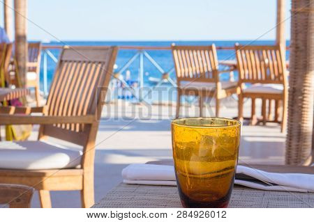 An Empty Orange Glass Standing On Table At Beach Cafe With Sea View