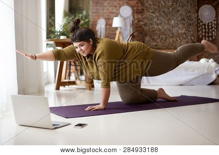 Obese Chubby Young European Female With Hair Knot Practicing Yoga Or Pilates Indoors On Mat, Doing E