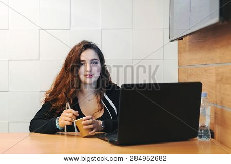 Young Beautiful Girl In Cafe Drinks Coffee. On The Table Is Laptop And Bottle Of Potable Water