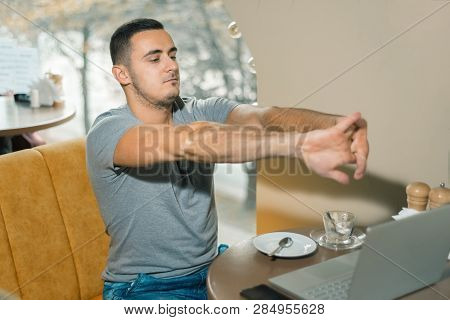 Young Guy Working In A Cafe. The Man Was Tired And Took A Break To Rest. Male Pulled His Hands Forwa