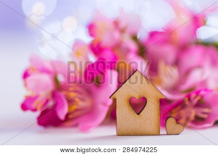 Closeup Wooden House With Hole In Form Of Heart With Tender Pink Cherry Flowers On Blurred Lilac Bac