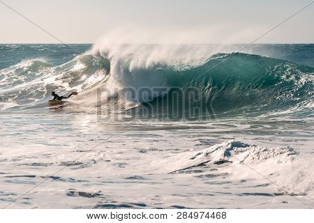 Man Surfing A Huge Wave That Chases Him, The Sunlight Reflects Golden On The Turquoise Surface Of Th