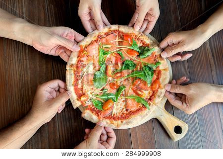People Hands Taking Slices Of Salmon Pizza With Rocket And Tomato.
High Angle Friend Group Hands Gra