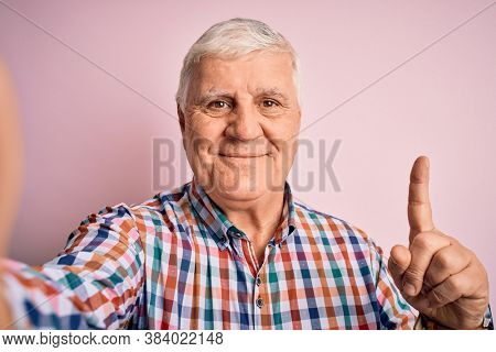 Senior handsome hoary man wearing casual shirt making selfie by the camera surprised with an idea or question pointing finger with happy face, number one