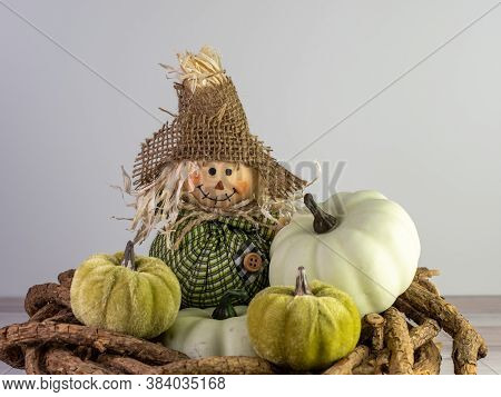 Mini Scarecrow With A Burlap Hat Sitting On A Wooden Wreath With Little Green Gourds Piled Around It
