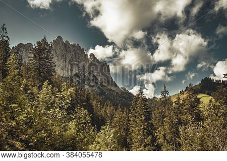 Idyllic View On Gastlosen Mountains In Switzerland With Forest In The Foreground And A Cloudy Sky In