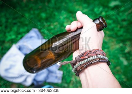 A Hand Of A Hippie, Hipster Holding A Bottle Of Alcohol, Beer. Young People With Alcohol Addiction C