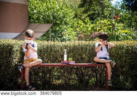 Coronavirus School Reopening Concept: A School Boys Sit On Bench In Front Of A School Wearing A Face