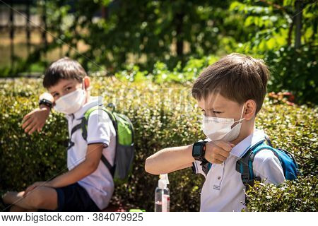 Coronavirus School Reopening Concept: A School Boys Sit On Bench In Front Of A School Wearing A Face