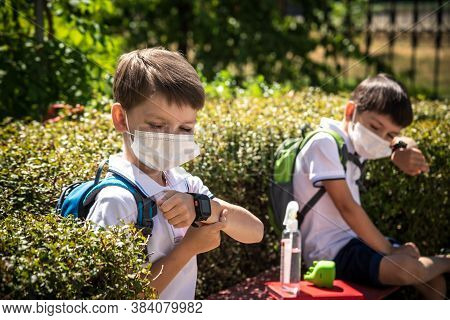 Coronavirus School Reopening Concept: A School Boys Sit On Bench In Front Of A School Wearing A Face