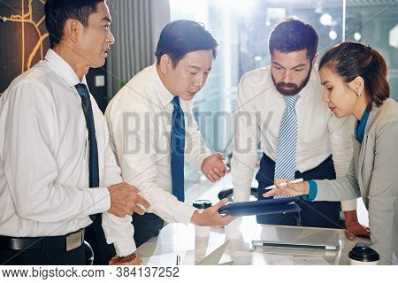 Multi-ethnic Business Team Gathered At Table To Discussing Financial Document On Tablet Computer And