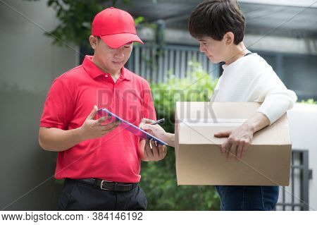 Asian Delivery Man In Red Uniform Delivering Parcel Box To Woman Recipient At Home With Recipient Si
