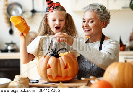 Cheerful Senior Woman And Amazed Girl Putting Toy Spider Into Jack O Lantern While Preparing For Hal