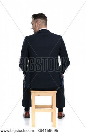 Back view of a businessman looking over his shoulder and sitting on a chair on white studio background