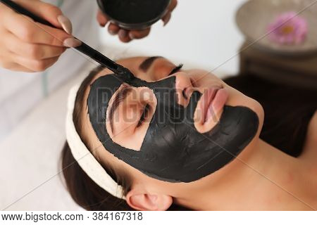 Closeup Of Unrecognizable Cosmetologist Applying Face Mask With Brush To Face Of Beautiful Woman Lyi