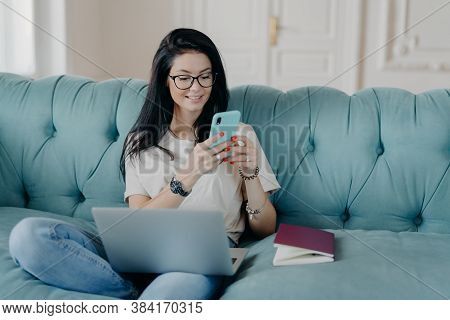 Happy Female Blogger Chats With Friends In Social Netwoks, Works On Laptop Computer, Poses In Cowork